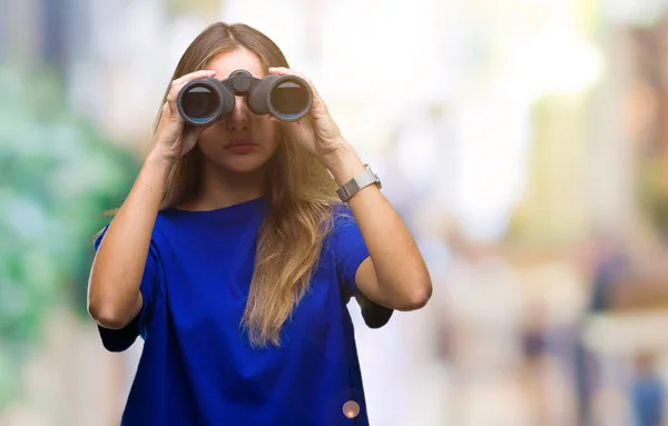年轻美丽的金发碧眼的女人通过双筒望远镜在孤立的背景 在聪明的脸上自信的表情思考严重 — 图库照片