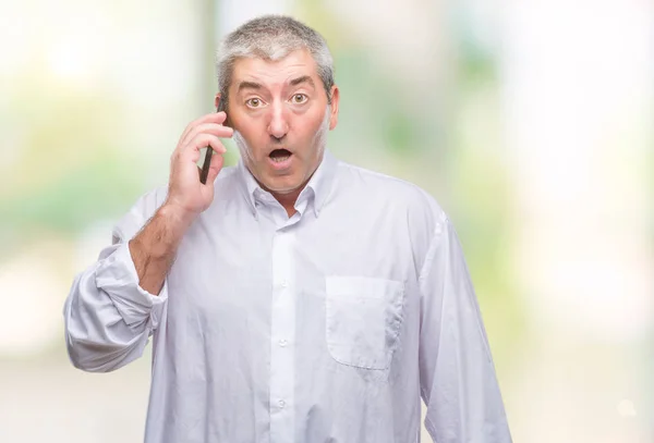 Handsome senior man talking on smartphone over isolated background scared in shock with a surprise face, afraid and excited with fear expression