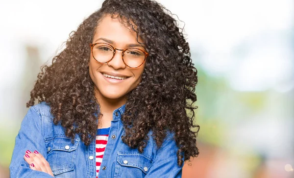 Young beautiful woman with curly hair wearing glasses happy face smiling with crossed arms looking at the camera. Positive person.