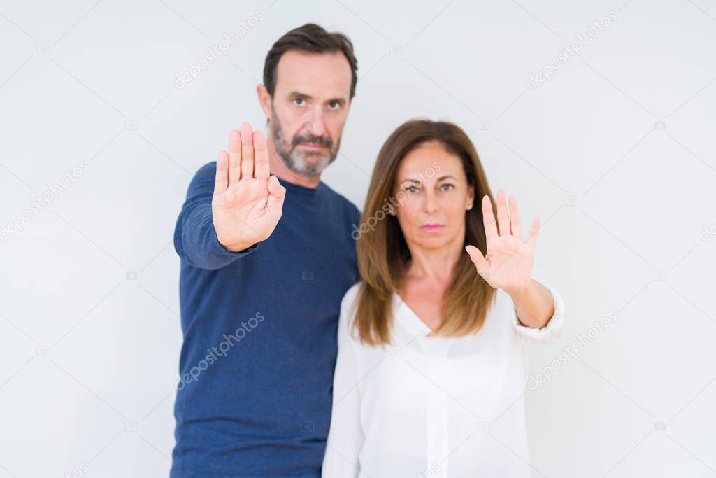 Beautiful middle age couple in love over isolated background doing stop sing with palm of the hand. Warning expression with negative and serious gesture on the face.