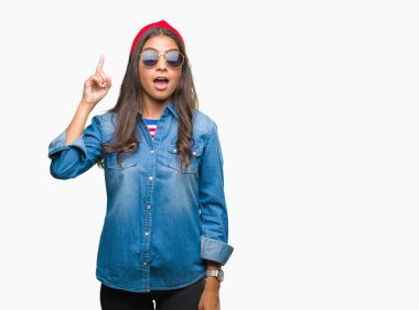 Genç güzel Arap kadın başarılı fikirle izole arka plan işaret parmağı üzerinde güneş gözlüğü takıyor. Çıktıktan ve mutlu. Bir numara.