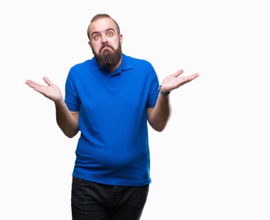 Üzerinde mavi gömlek giymiş genç beyaz hipster adam arka plan clueless ve şaşkın bir ifadeyle kollar ve eller kaldırdı izole. Şüphe kavramı.
