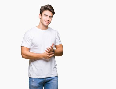 Arka plan eller üzerinde beyaz t-shirt giyen genç yakışıklı adam birlikte izole ve rahat ve neşeli gülümseyen parmak çarpı işareti. Başarı ve iyimser