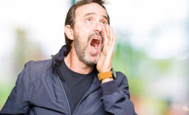 Orta yaş yakışıklı adam bir ceket giyen bağırarak ve ağızda el ile yan yüksek sesle bağırıyor. İletişim kavramı.