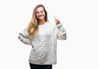 Kış kazak ve güneş gözlüğü ve parmak gülümseyen süre bir numara ile kendinden emin ve mutlu yukarıyı gösteren izole arka plan üzerinde giyen genç güzel sarışın kadın.