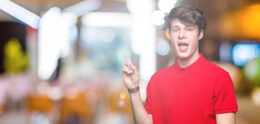 Kameraya bakarak yan el ve parmak ile işaret yüzünde kocaman bir gülümseme ile izole arka plan üzerinde kırmızı t-shirt giyen genç yakışıklı adam.