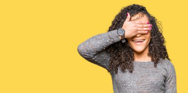 Gözler için sürpriz kapsayan yüz el ile kıvırcık saçlı giyen genç güzel gri kazak gülümseyen kadın ve ile gülüyor. Kör kavramı.