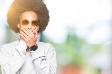 Afrikalı-Amerikalı genç afro saçlı ağız hata için elleriyle kapsayan şok güneş gözlüğü takıyor. Gizli kavramı.