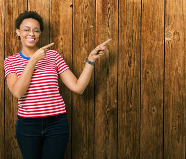Güzel genç Afro-Amerikan kadın gülümseyerek ve iki elleri ve parmakları ile tarafına işaret kamera bakarak izole arka plan üzerinde gözlük.