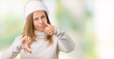 Üzerinde kış kazak ve şapka giyen güzel orta yaş kadın arka plan yapmaya başparmak yukarı ve aşağı anlaşmazlık ve anlaşma ifade izole. Deli çatışma