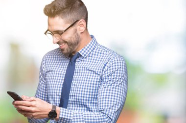 Genç iş adamı izole arka plan üzerinde duran ve diş gösterilen kendine güvenen bir gülümsemeyle gülümseyerek mutlu bir yüz ile Smartphone kullanarak