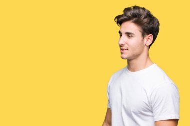 Uzak tarafına yüzünde, doğal ifade gülümseme ile seyir izole arka plan üzerinde beyaz t-shirt giyen genç yakışıklı adam. Kendine güvenen gülüyor.