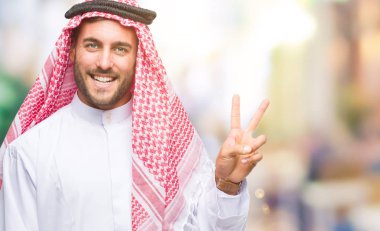 Mutlu yüz zafer işareti yaparken kameraya göz kırpıyor ile gülümseyen izole arka plan üzerinde keffiyeh giyen genç yakışıklı adam. İki numaralı.