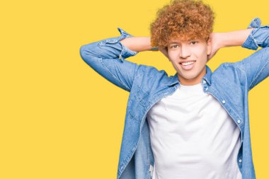 Genç yakışıklı adam ile afro saç giyen denim ceket rahatlatıcı ve baş ve boyun arkasında silah ve eller ile germe, gülümseyen mutlu