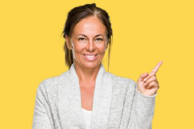 Kameraya bakarak yan el ve parmak ile işaret yüzünde kocaman bir gülümseme ile izole arka plan üzerinde kış kazak giyen güzel orta yaş yetişkin kadın.