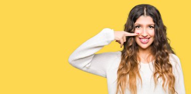 Beyaz kazak giyen genç güzel kadın yüz ve burun, neşeli gülümseyerek el parmak ile işaret