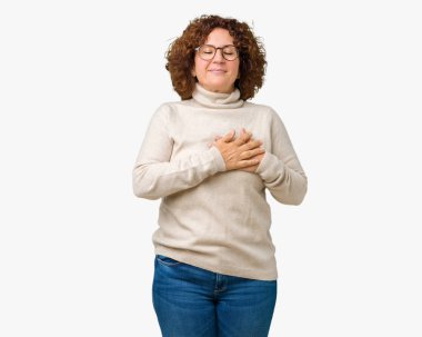 Boğazlı kazak ve gözlük ile kapalı gözler göğüs ellerinde ve yüzünde minnettar jest ile gülümseyen izole arka plan üzerinde giyen güzel orta ager üst düzey kadın. Sağlık kavramı.