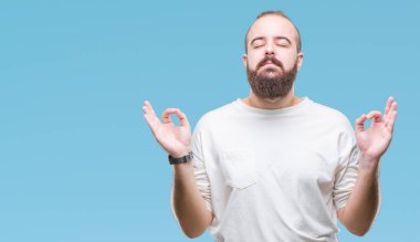 İzole arka plan üzerinde rahat t-shirt giyen genç beyaz hipster adam rahatla ve gülümseyen gözlerle kapalı parmak jestle meditasyon yapıyor. Yoga kavramı.