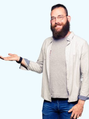 Neşeli sunulması ve kameraya bakarak avucunun ile işaret gülümseyen gözlüklü genç sarışın adam.