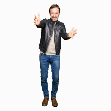 Orta yaş yakışıklı adam sarılmak için kollarını açarak gülümseyerek kameraya bakarak siyah deri ceket giyiyor. Neşeli ifade kucaklayan mutluluk.