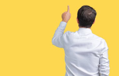 Yakışıklı orta yaş zarif üst düzey iş adam gözlük izole üzerinden geriye doğru arkasında parmak eliyle işaret Posing arka plan