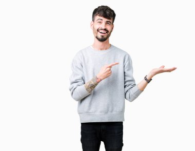 Genç yakışıklı adam izole arka plan üzerinde Sweatshirt giyiyor hayran ve kameraya gülümseyen el ile sunmak ve parmak ile işaret.
