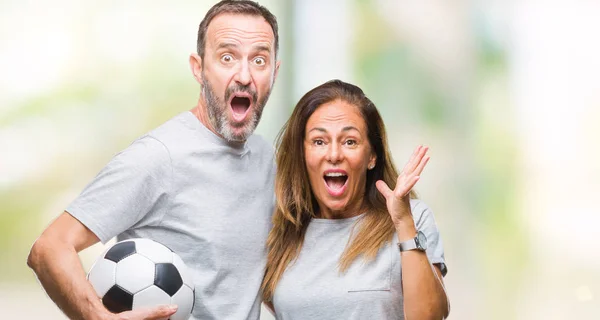 Middle age hispanic couple holding football soccer ball over isolated background very happy and excited, winner expression celebrating victory screaming with big smile and raised hands