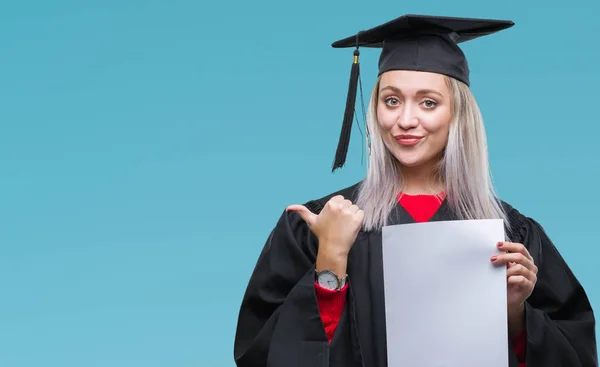 指していると幸せそうな顔を笑顔で側まで親指で示す分離の背景上の学位を保持する大学院の制服を着て若いブロンドの女性 — ストック写真