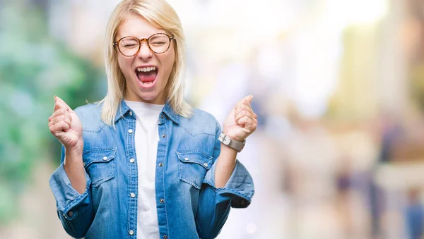 年轻漂亮的金发女人戴着眼镜在孤立的背景下兴奋的成功与手臂举起庆祝胜利微笑 赢家理念 — 图库照片