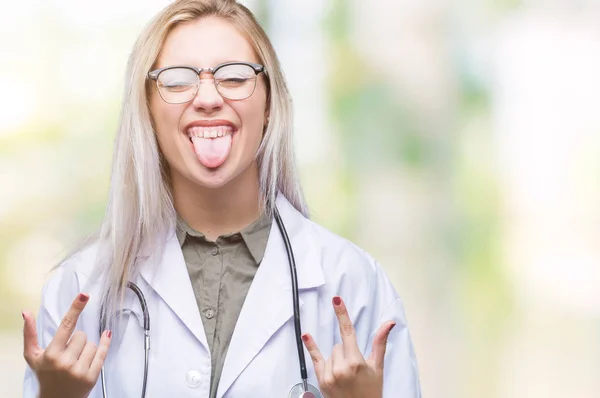 Young blonde doctor woman over isolated background shouting with crazy expression doing rock symbol with hands up. Music star. Heavy concept.