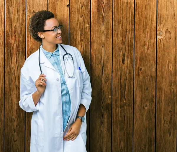年轻的非洲女医生穿着医疗外套在孤立的背景看着一边面带微笑 自然的表情 笑自信 — 图库照片