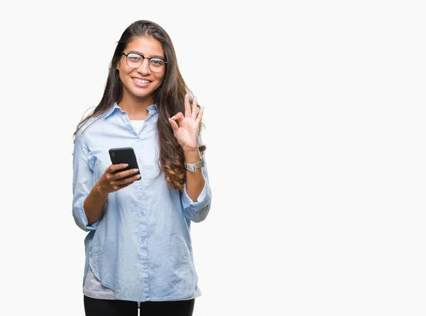 優秀なシンボルの指で サインをして孤立の背景にスマート フォンを使用して若いアラブ美人のテキスト メッセージ — ストック写真