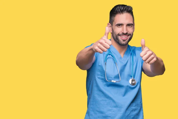 英俊的年轻医生外科医生在孤立的背景下批准做积极的手势用手 竖起大拇指微笑和快乐的成功 看着镜头 赢家的手势 — 图库照片