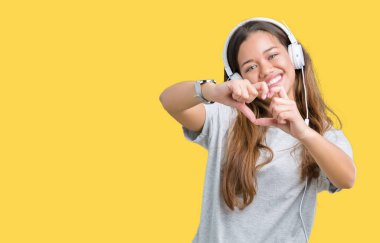 Kalp simgesi ve elleriyle şekil gösterilen aşık gülümseyen izole arka plan üzerinde müzik kulaklık giyen genç güzel kadın. Romantik kavramı.