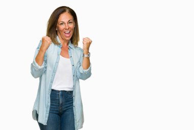 Gülümseyen ve başarı için çığlık izole arka plan çok mutlu ve heyecanlı kaldırdı, silah ile kazanan jest yapıyor üzerinde rahat kot gömlek giymiş orta yaş yetişkin bir kadın. Kutlama kavramı.