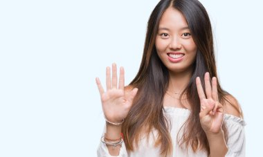 Genç Asyalı kadın gösterilen ve parmakları ile işaret izole arka plan üzerinde kendinden emin ve mutlu gülümseyerek süre sekiz numara.