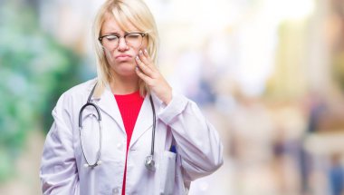Diş ağrısı veya dişlerde dişlerle ilgili hastalık nedeniyle ağız acı ifadesi ile el ile dokunmak izole arka plan üzerinde tıbbi üniforma giyen genç güzel sarışın doktor kadın. Diş hekimi kavramı.