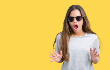 Genç güzel esmer kadın korkuyor ve şok sürpriz ifade, korku ve heyecan yüz ile izole arka plan üzerinde güneş gözlüğü takıyor.