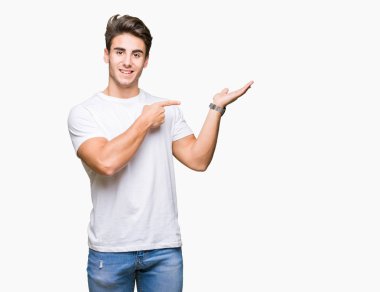 Hayret ve el ile sunulması ve parmak ile işaret ederken kameraya gülümseyen izole arka plan üzerinde beyaz t-shirt giyen genç yakışıklı adam.
