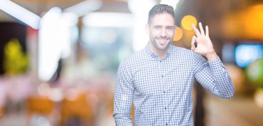 Gülümseyen izole arka plan üzerinde genç yakışıklı adam el ve parmaklar ok işaretiyle yapıyor olumlu. Başarılı ifade.