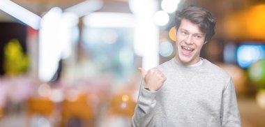 Seyir ve başparmak yanında yukarıyı mutlu yüz ile gülümseyen izole arka plan üzerinde sweatshirt giyen genç yakışıklı sportif adam.