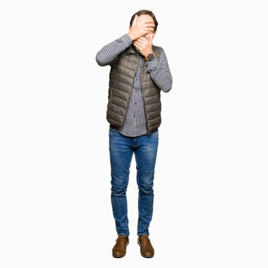 Orta yaş yakışıklı adam giyen kış kapsayan gözleri yelek ve ağız şaşırttı ve şok elleriyle. Duygu gizleme