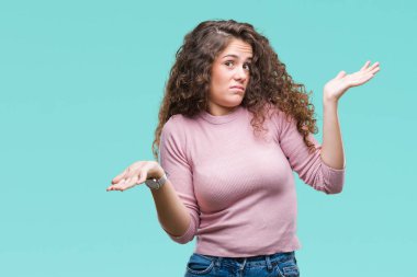 Güzel esmer kıvırcık saçlı Genç kız üzerinde pembe kazak giyiyor arka plan clueless ve şaşkın bir ifadeyle kollar ve eller kaldırdı izole. Şüphe kavramı.