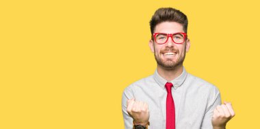 Kutluyor gözlük takan genç yakışıklı iş adamı şaşırttı ve başarı için kaldırdı kollarını açarak hayret ve gözleri açık. Kazanan kavramı.