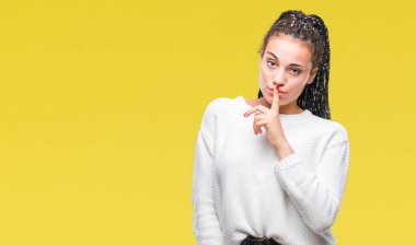 Genç örgülü saç Afro-Amerikan kız dudaklarında parmak ile sessiz olmanı izole arka plan üzerinde kış kazak giyiyor. Sessizlik ve gizli kavramı.