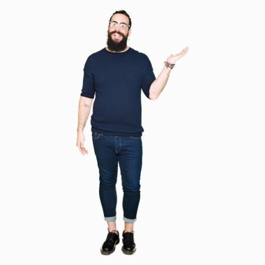 Uzun saç ve sakal neşeli sunulması ve kameraya bakarak avucunun ile işaret gülümseyen gözlüklü genç hipster adamla.