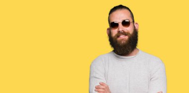 Kameraya bakarak çapraz silah ile gülümseyen güneş gözlüğü mutlu yüz giyen genç hipster adam. Olumlu bir kişi.