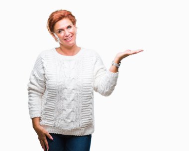 Neşeli sunulması ve kameraya bakarak avucunun ile işaret gülümseyen izole arka plan üzerinde kış kazak giyen Atrractive üst düzey beyaz Kızıl saçlı kadın.