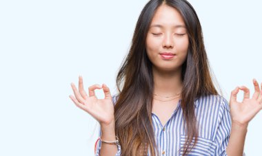 Genç Asyalı kadın izole arka plan üzerinde dinlenmek ve gülümseyen gözlerle parmak ile meditasyon jest yapıyor kapalı. Yoga kavramı.