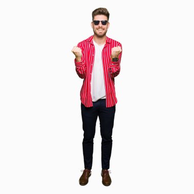 Yakışıklı delikanlı kutluyor güneş gözlüğü takıyor şaşırttı ve silah ile başarı için yükseltilmiş ve açık gözler hayrete düşürdü. Kazanan kavramı.